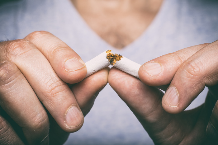 Mãos a partir um cigarro ao meio.