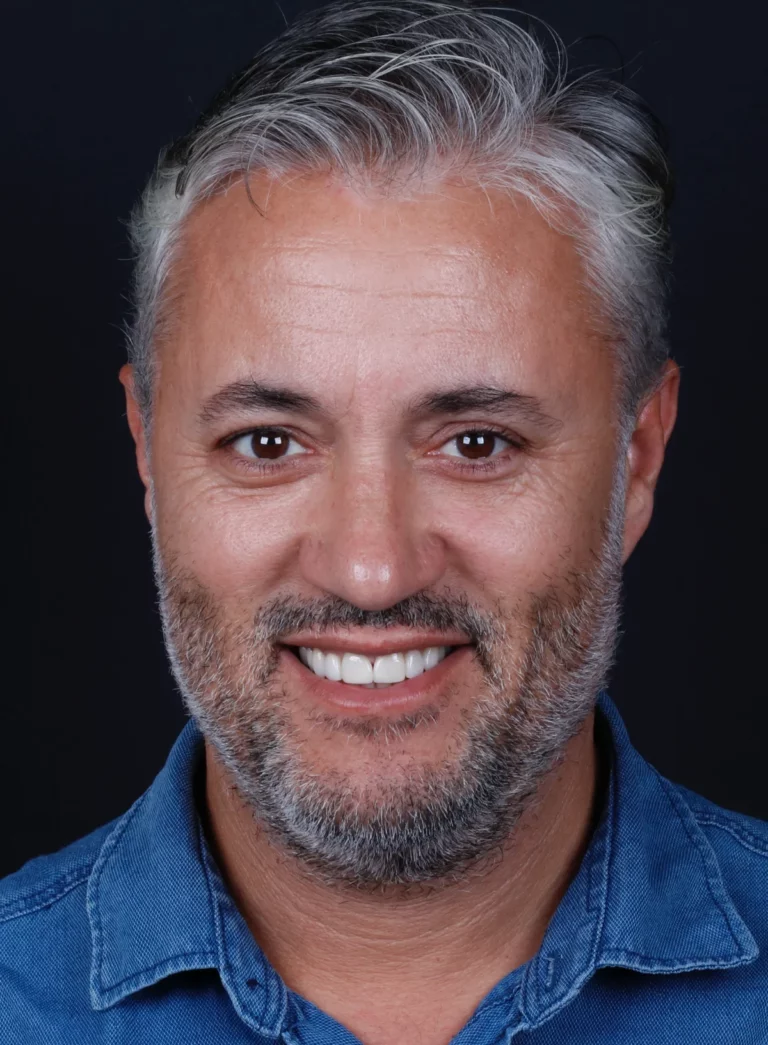 Retrato de homem de cabelo grisalho e barba, a sorrir, com camisa azul.
