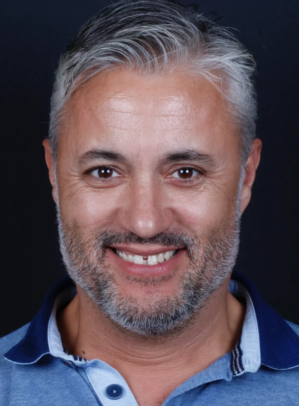 Retrato frontal de um homem de cabelo grisalho a sorrir.