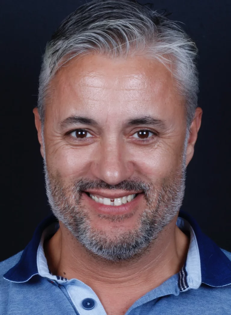 Retrato frontal de um homem de cabelo grisalho a sorrir.