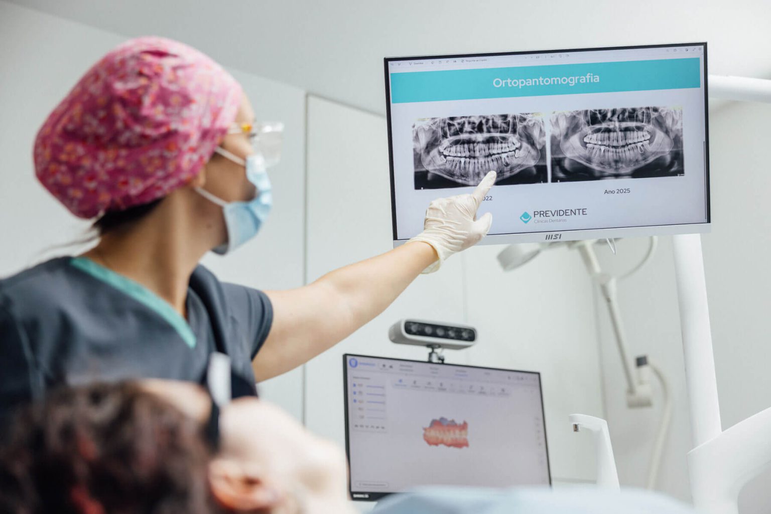Profissional a mostrar uma radiografia panorâmica dentária num monitor durante a consulta.