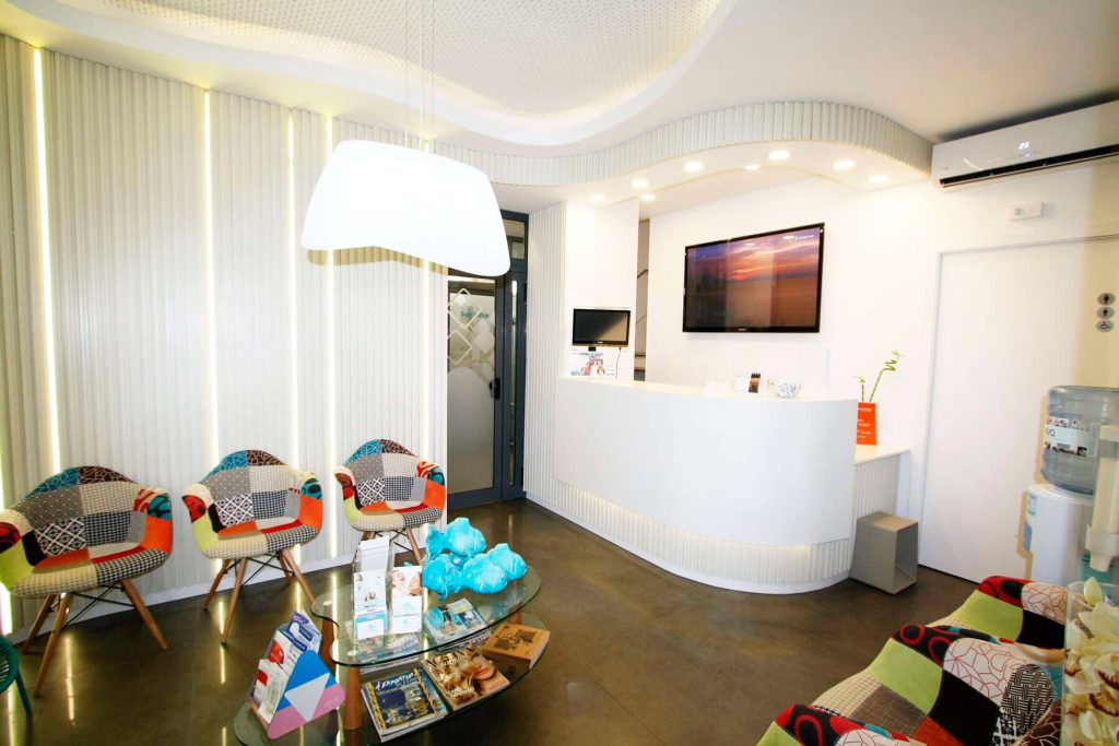 Recepção e sala de espera de uma clínica dentária, com cadeiras coloridas.