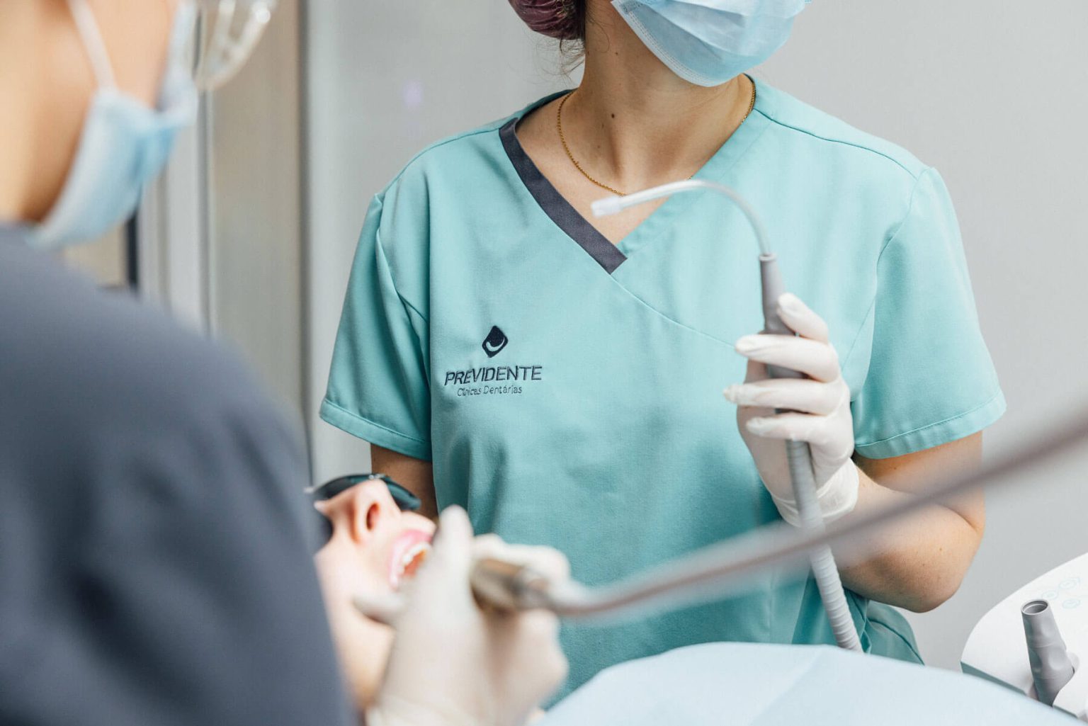 Dois profissionais com máscaras e luvas junto de uma pessoa na cadeira dentária.