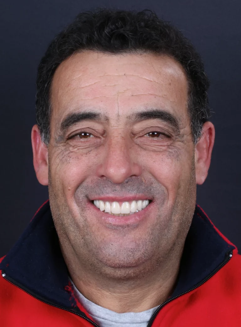Retrato frontal de homem de cabelo escuro, a sorrir, com casaco vermelho.