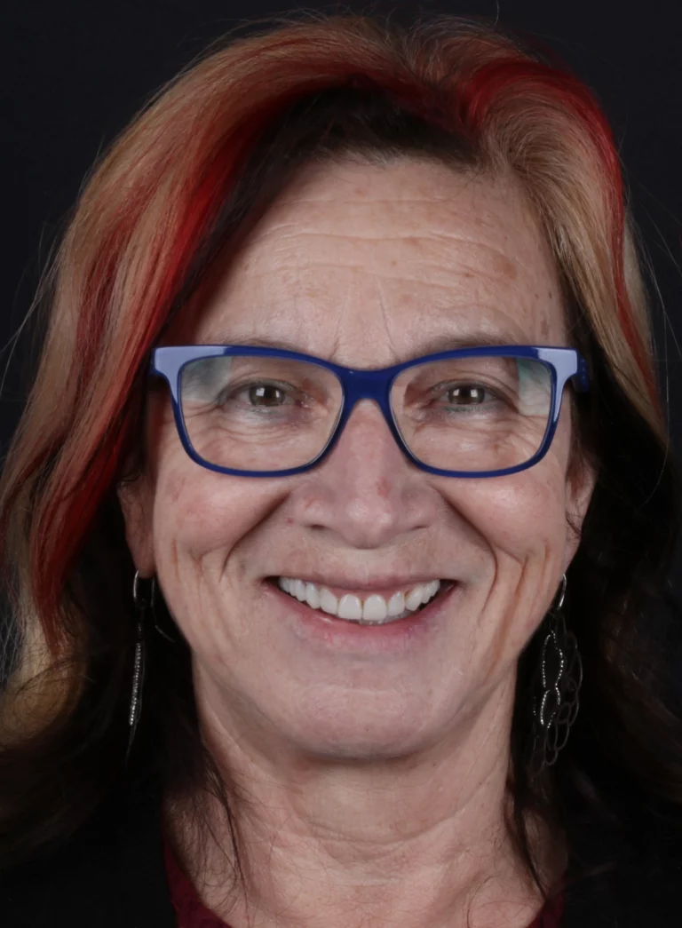 Retrato frontal de mulher com óculos azuis, a sorrir.
