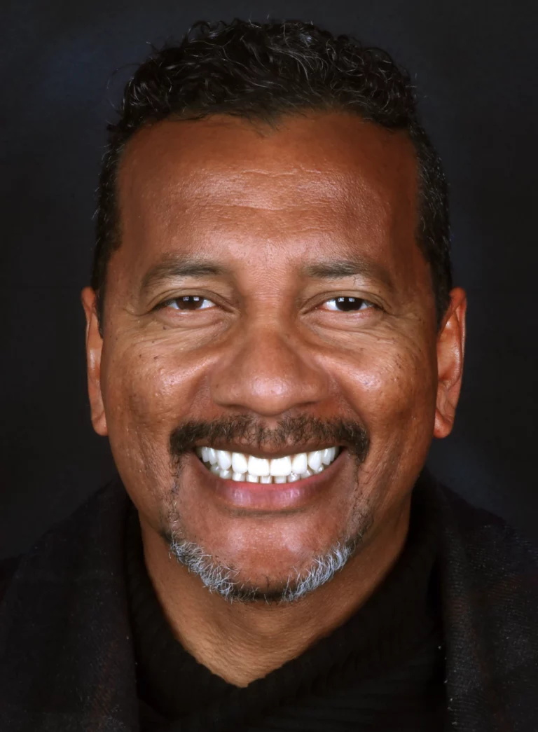 Retrato frontal de um homem de bigode a sorrir, com os dentes visíveis.