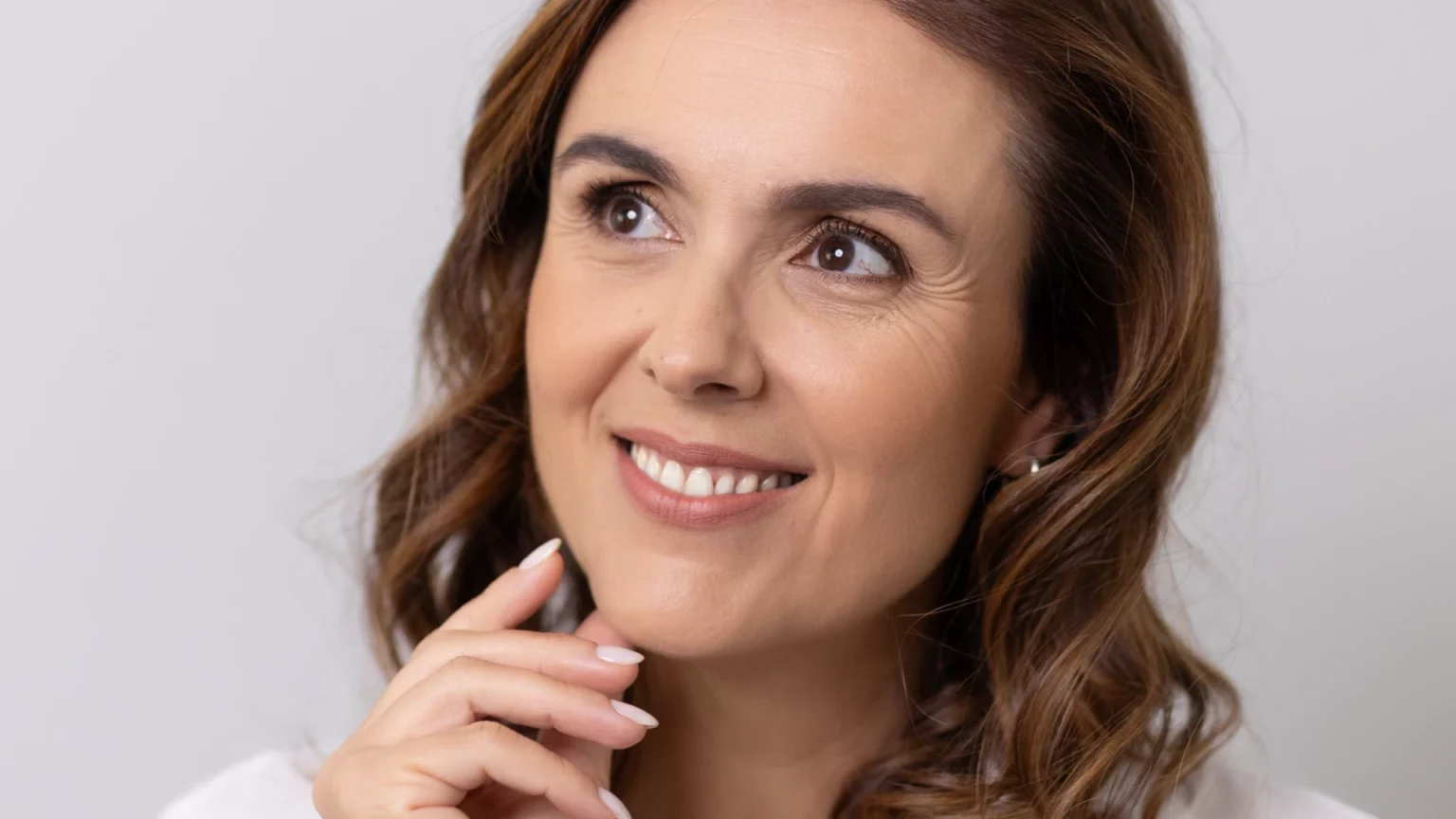 Mulher a sorrir, com uma mão junto ao queixo.