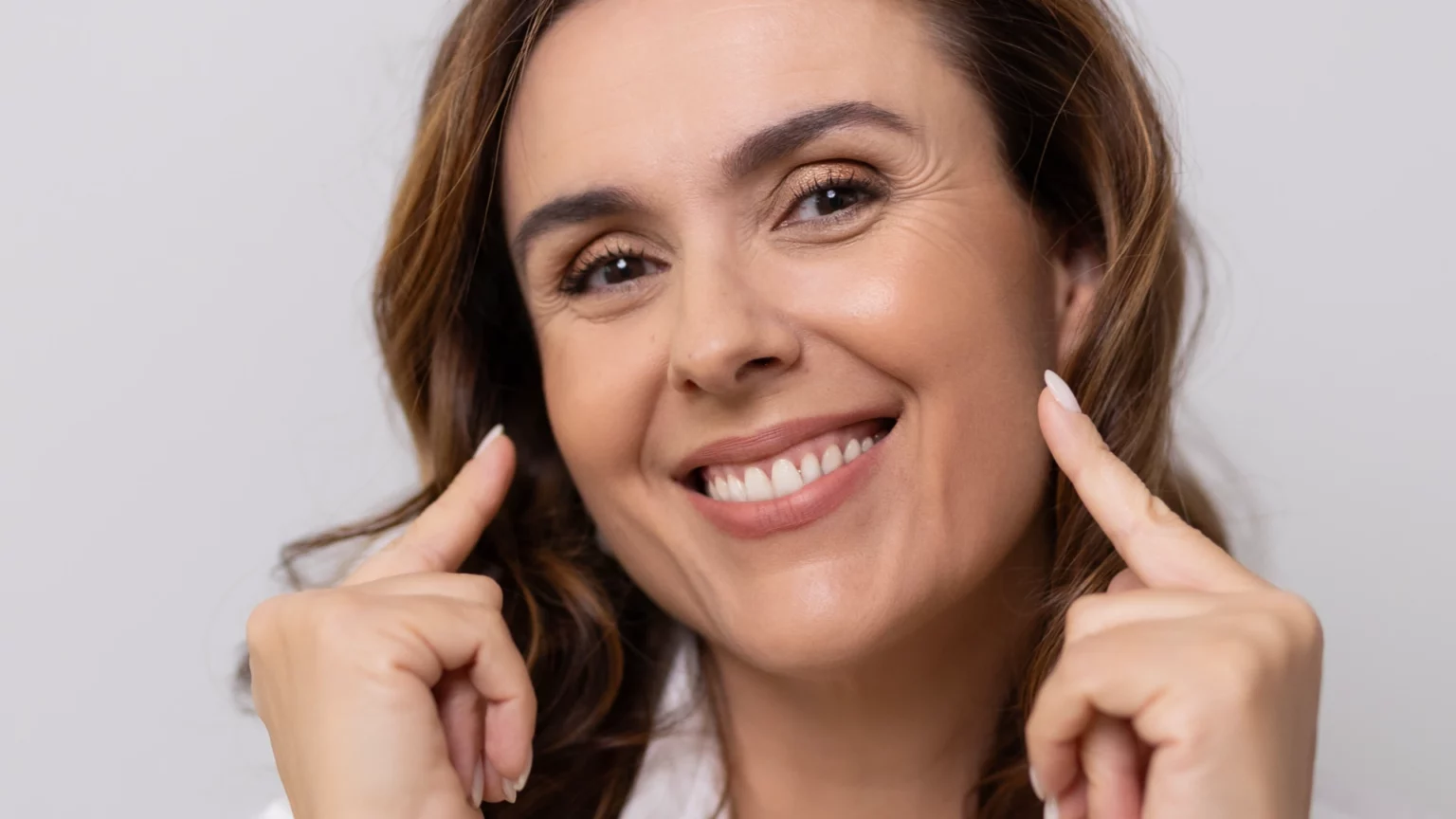 Mulher a sorrir e a apontar para as faces com os dedos indicadores.