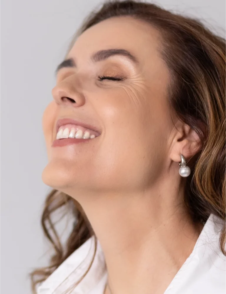 Mulher a sorrir com os olhos fechados e o rosto voltado para cima.