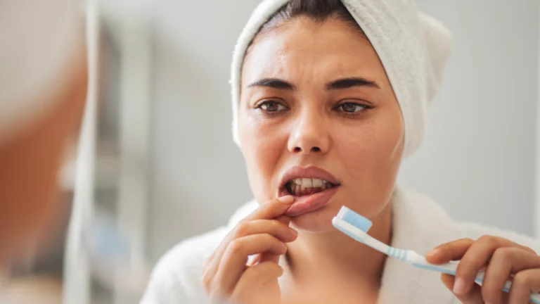 Mulher a observar a gengiva inferior ao espelho, segurando uma escova de dentes