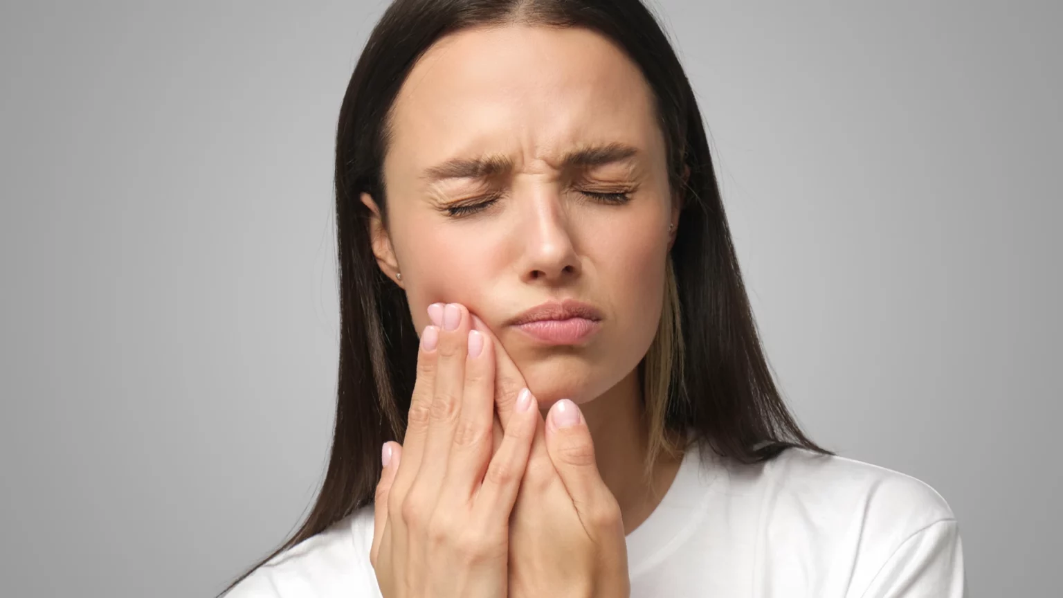 Mulher de olhos fechados com a mão encostada ao maxilar.