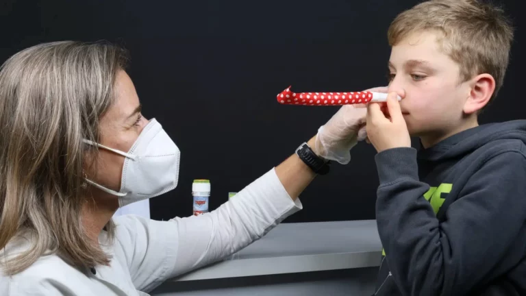 Profissional a acompanhar uma criança que segura um tubo vermelho junto ao rosto.