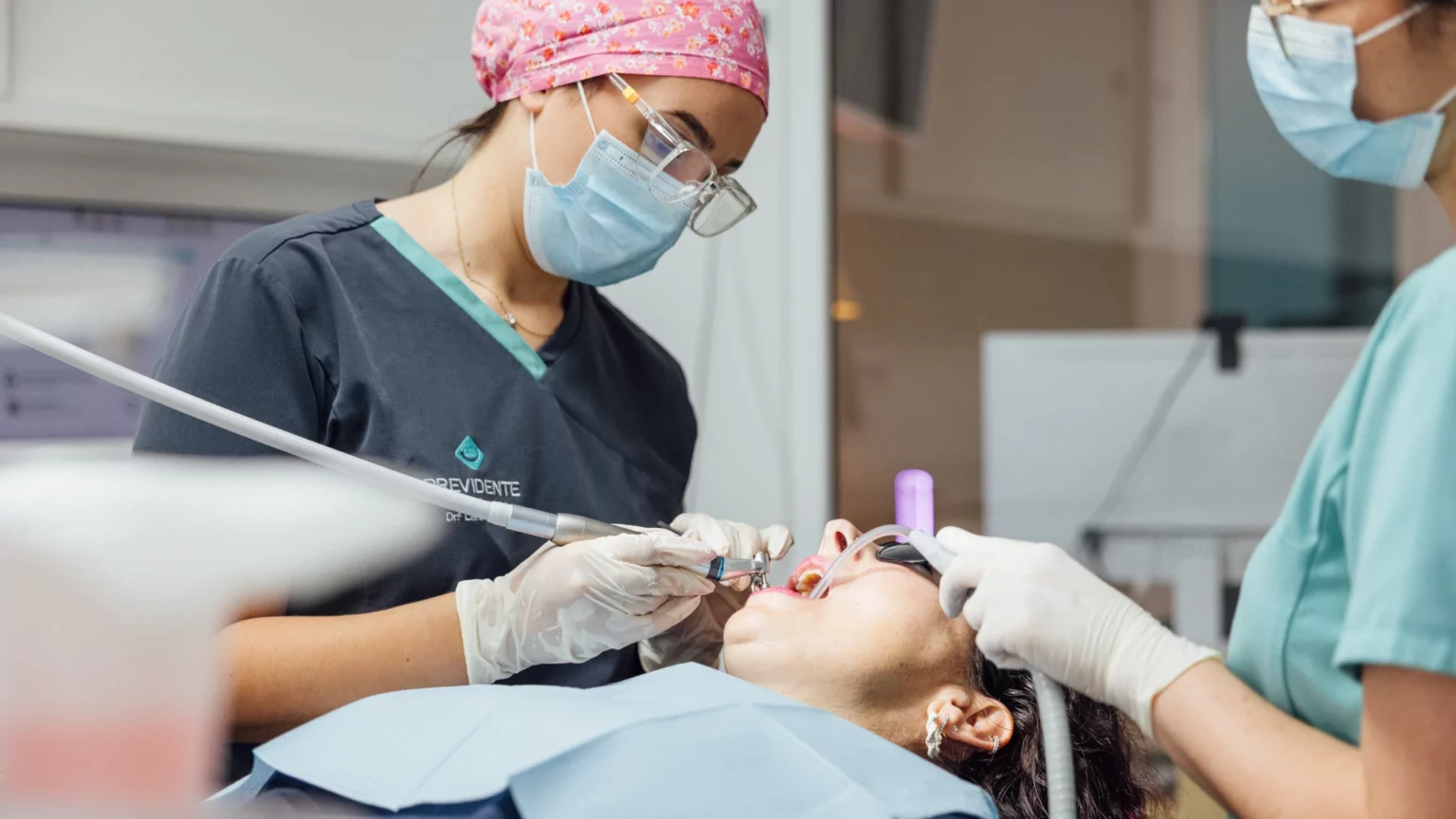 Dois profissionais com máscaras e luvas a observar a boca de uma pessoa na cadeira dentária.