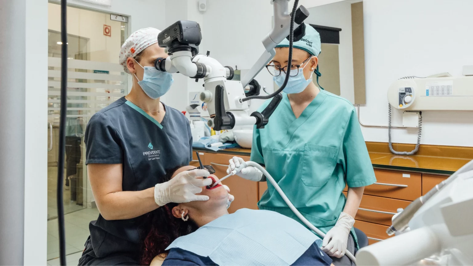 Dois profissionais junto de uma pessoa na cadeira dentária, com um microscópio.