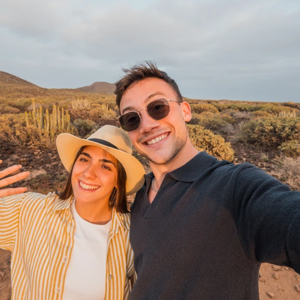 Homem e mulher a sorrir ao ar livre, numa paisagem com cactos.