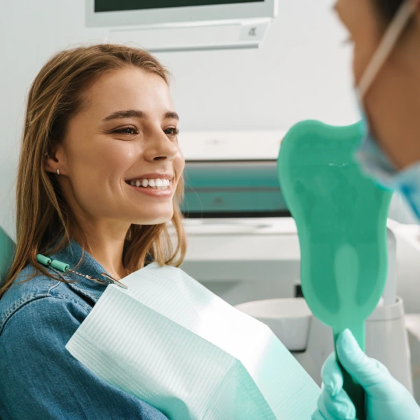 Mulher a sorrir na cadeira dentária, com um espelho de mão à sua frente.